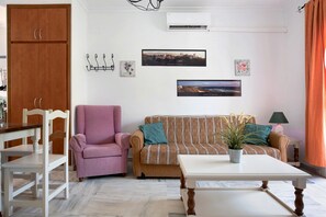 A living room with a sofa, armchair, dining table, and a potted plant.