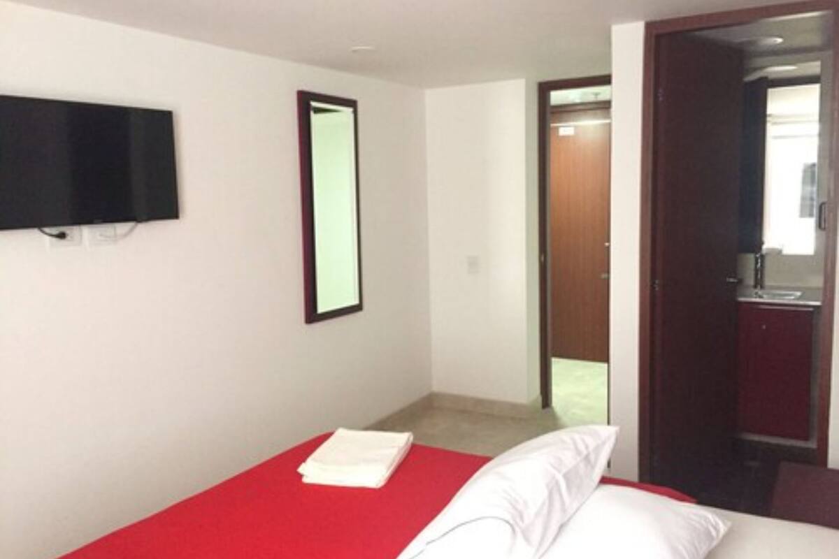 A hotel room with a bed, a TV mounted on the wall, and a door leading to a bathroom.