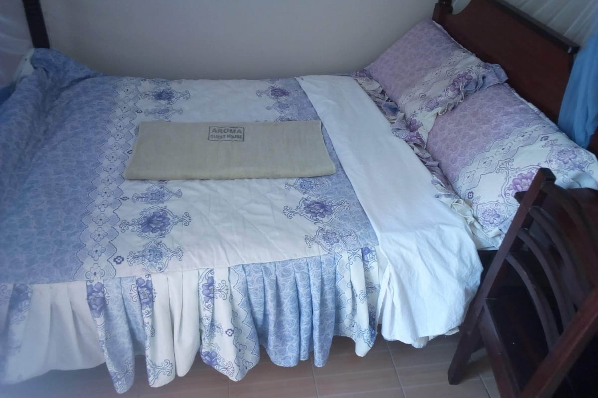 Ein Bett mit floralem Bettbezug und Kissen, einer beigen Decke und einem Holzkopfschild.