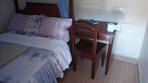 Une chambre à coucher avec un lit, une chaise en bois, une petite table et une prise électrique au mur.