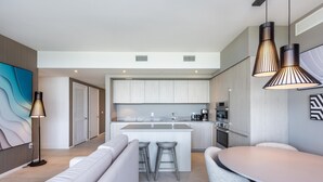 Una cocina moderna con armarios blancos, una isla central y electrodomésticos de acero inoxidable. Hay un comedor con una mesa redonda y sillas grises.