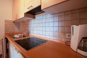 A kitchen with a built-in stovetop, a coffee maker, and wooden cabinets. - Cosy Apartment 1 "Zur Sonne" with Mountain View & Garden (Lajen)
