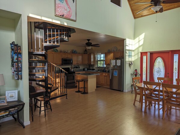 A spacious kitchen with wooden cabinets, a stainless steel refrigerator, and a built-in oven. There is a wooden staircase leading to an upper level, and a dining area with wooden chairs and a table.