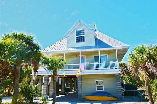 A two-story house with a balcony, surrounded by palm trees.