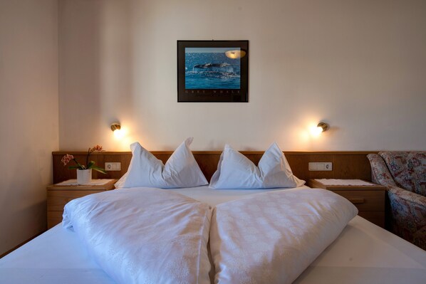 Une chambre d’hôtel comprenant un lit, deux tables de chevet, une petite table, un tableau représentant une baleine accroché au mur, et deux lampes murales.