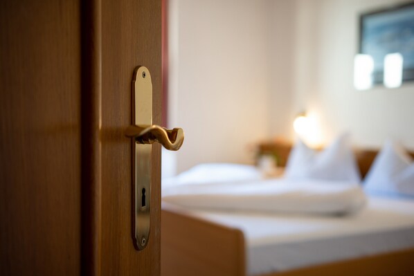 Une chambre d’hôtel avec une porte en bois, un lit avec une literie blanche et une table de chevet avec une lampe.