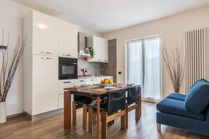 Une cuisine moderne avec des meubles blancs, une table à manger avec des chaises et un canapé bleu dans l’espace salon.