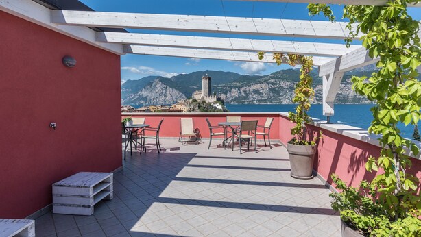 A terrace with outdoor seating, a view of the sea, and a mountain backdrop.