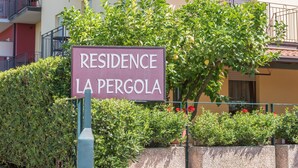 A sign for 'Residence La Pergola' with a hedge and a building in the background.