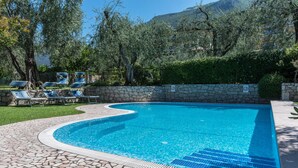A swimming pool with a stone border, lounge chairs, and a stone wall with a no swimming sign.