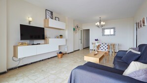 Uma sala de estar moderna com televisão de tela plana, estantes embutidas, um sofá, uma mesa de jantar e um lustre.