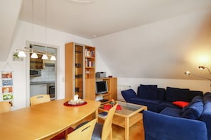 A modern living room with a dining table, blue sofa, and a bookshelf.