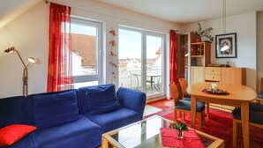 Una sala de estar con un sofá azul, una mesa de centro de cristal, una mesa de comedor con sillas y vistas al exterior a través de amplios ventanales.