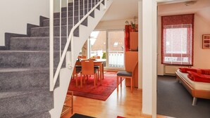 Una escalera conduce a un área de comedor con un tapete rojo, un sofá y una ventana con cortinas.