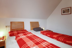 A room with two beds, each with a wooden headboard, a nightstand, and a wall-mounted picture.