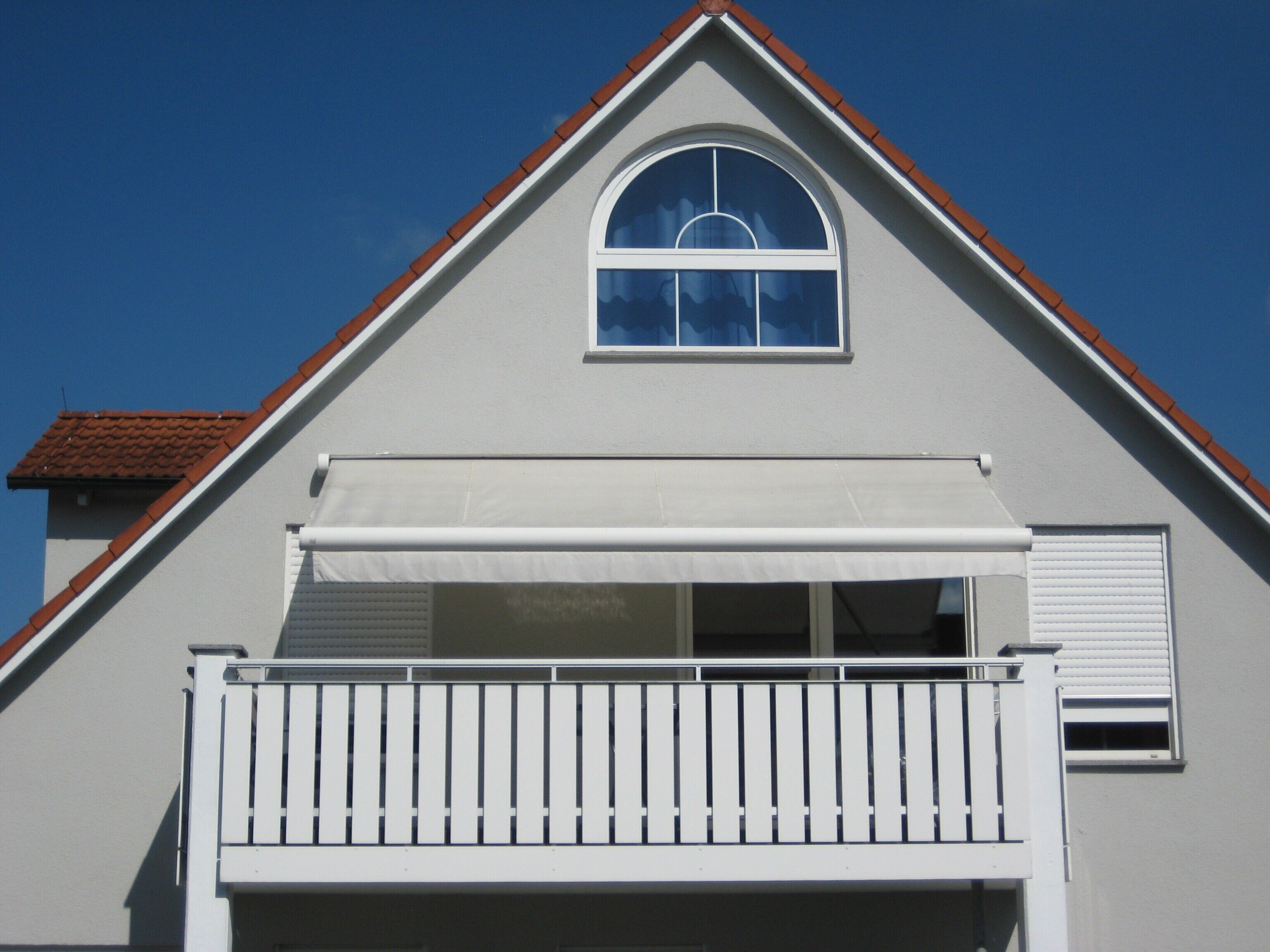 A residential building with a gabled roof, a balcony with white railings, and a garage door.