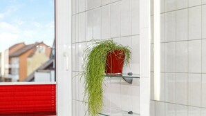 Un baño con paredes de azulejos blancos, un inodoro rojo y una planta verde colgante.