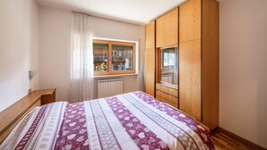 Camera da letto con un letto, un armadio in legno, una finestra e un termosifone.