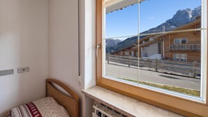 Una stanza con un letto di legno, una finestra vista montagne e una capanna di legno sullo sfondo.