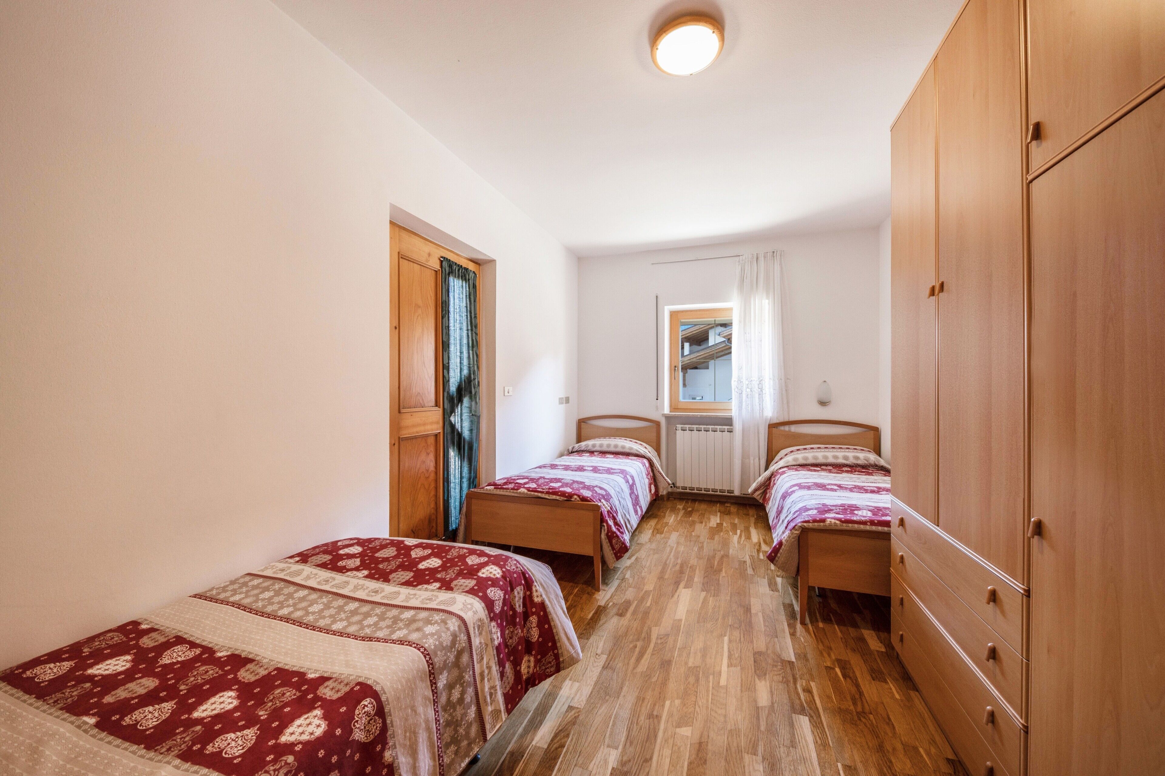 Un dormitorio con dos camas individuales, un armario de madera y una ventana con cortinas.
