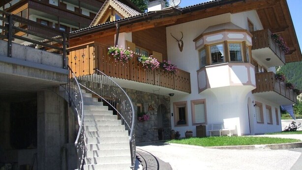 Un chalet a due piani con una scala in pietra, balconi in legno e un'antenna per gli sci.