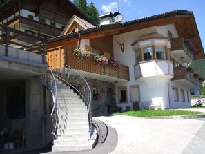 A two-story chalet with a stone staircase, wooden balconies, and a ski antenna.