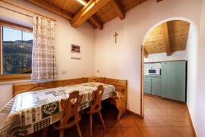 Un coin repas avec une table et des chaises en bois, une fenêtre offrant une vue agréable, une cuisine avec des meubles de couleur turquoise et un plafond en bois.