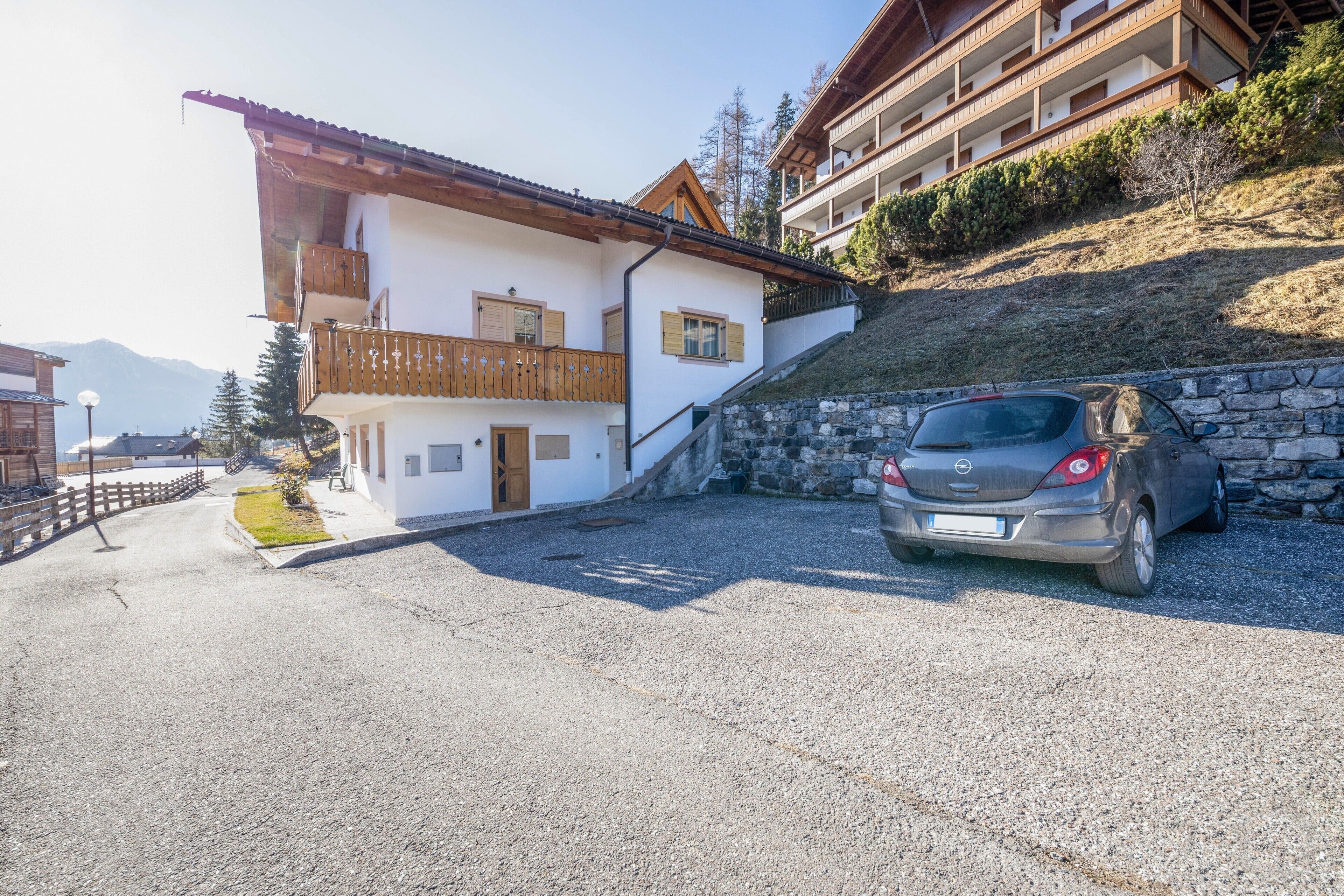 Ein zweistöckiges Gebäude mit Balkon, Steinmauer und geparktem Auto.