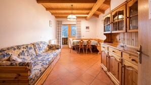 Una sala de estar con sofá, armarios de madera, una mesa de comedor y una ventana con cortinas.