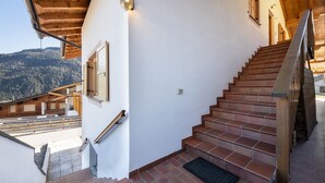 Una escalera con barandilla de madera, un felpudo negro y vistas a un paisaje montañoso.