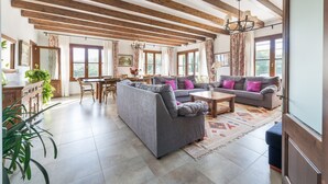 A spacious living room with a high ceiling, wooden beams, a dining area, and large windows. - Rural Idyll Villa "Sa Pleta" with Pool (Petra)
