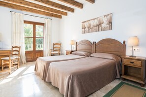 A double room with two beds, wooden headboards, a desk, chairs, a nightstand, and a window with curtains. - Rural Idyll Villa "Sa Pleta" with Pool (Petra)