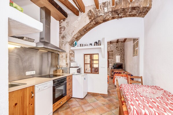 A compact kitchen with modern appliances, a dining area with a patterned tablecloth, and a rustic stone wall.