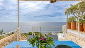 A terrace with a view of the sea, a table with a plant, and a railing.