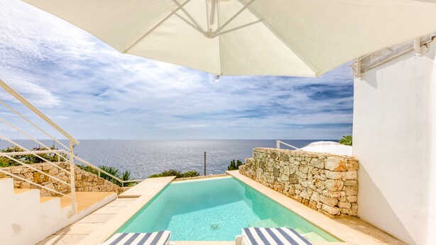 A swimming pool with a stone wall and a view of the sea.