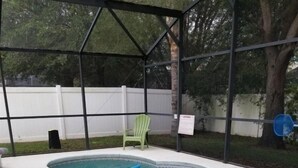 A swimming pool with a curved edge, surrounded by a covered area with a green chair and a blue pool float. - Rising Star in Clermont (Clermont)