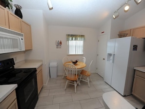 A compact kitchen with white cabinets, a black stove, a white refrigerator, and a dining table with two chairs. - Dream in Clermont (Clermont)