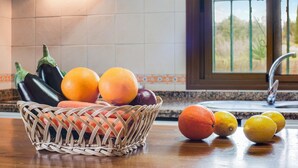 Una cocina con una cesta de mimbre llena de frutas y verduras, una encimera y una ventana con vistas a zonas verdes.