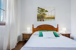 Un dormitorio con cama de madera, dos mesitas de noche con lámparas, una ventana con cortinas y un cuadro en la pared.