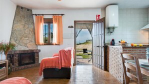 Habitación con chimenea, pared de piedra, vista a través de una puerta abierta y zona de cocina con calentador de agua.