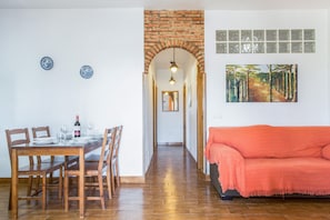 Comedor con una mesa de madera dispuesta para cuatro personas, un arco de ladrillo y un cuadro de un sendero forestal en la pared.