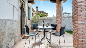 Un patio con una mesa redonda, cuatro sillas, una botella de vino y una copa de vino.