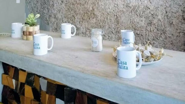 A modern kitchen with a stone backsplash, wooden ceiling beams, and a bar area with white mugs labeled "Casa Tulita". - Gorgeous Suite w/Premium Ammenties in Downtown (Valladolid)