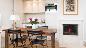 A dining area with a wooden table and four chairs, a vase with flowers, and a white cabinet with a microwave above it.
