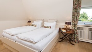 A bedroom with two single beds, a small wooden table with a lamp, and a window with floral curtains.