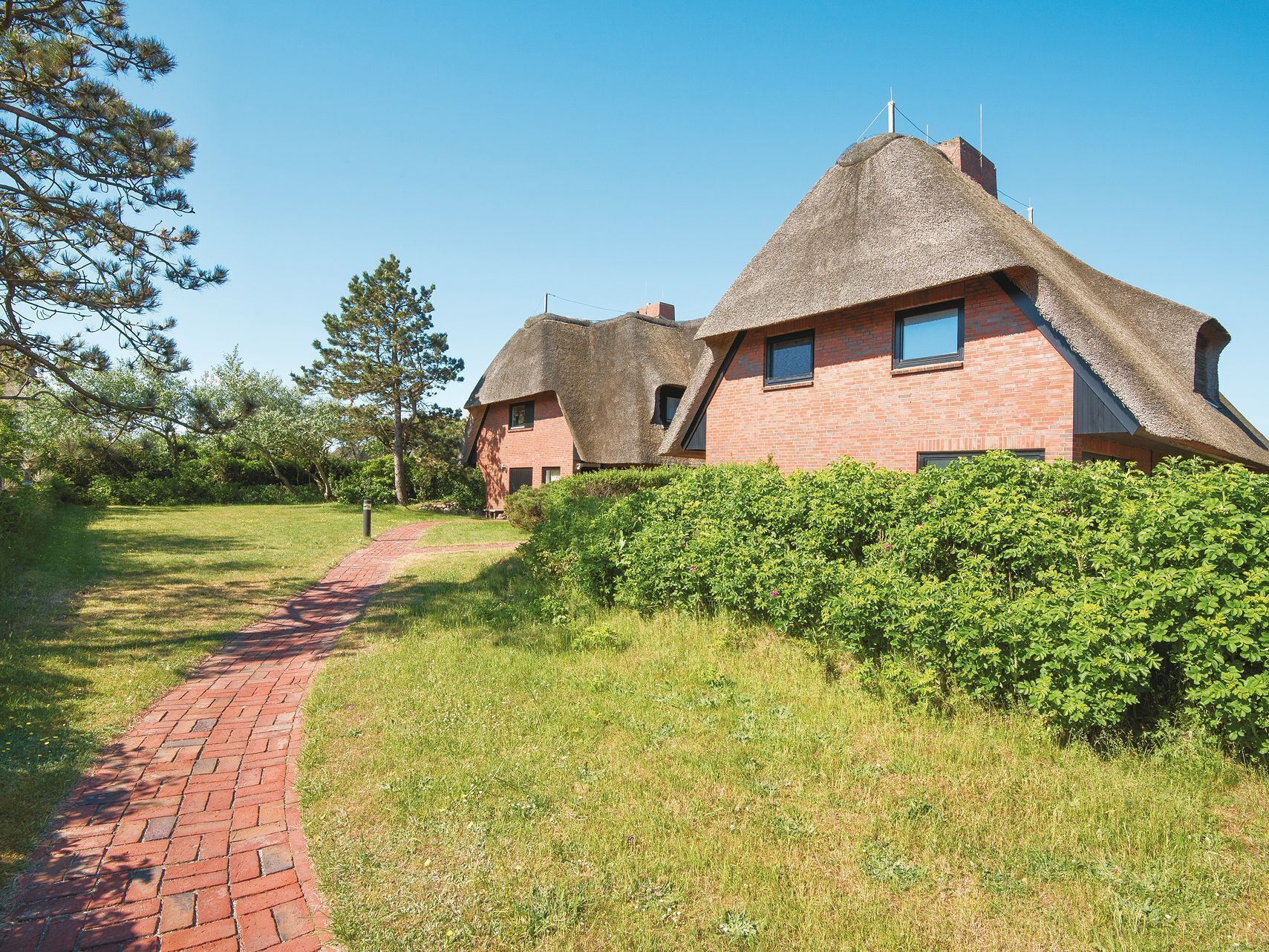 A traditional thatched-roof house with a brick exterior, surrounded by a hedge and a brick pathway.