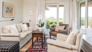 A living room with a beige sofa, a brown armchair, a coffee table, and a patterned rug. There is a potted orchid on the coffee table.
