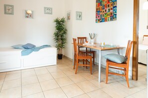 A small, clean room with a bed, a dining table with chairs, a potted plant, and a colorful wall art piece.