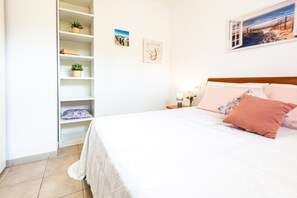 A bedroom with a bed, a nightstand, a shelf with plants, and a wall with a picture.