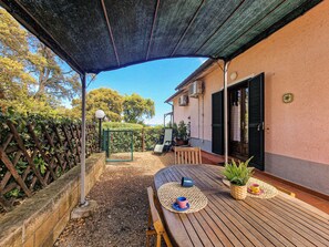 A covered patio area with a wooden table, a bench, and a potted plant.